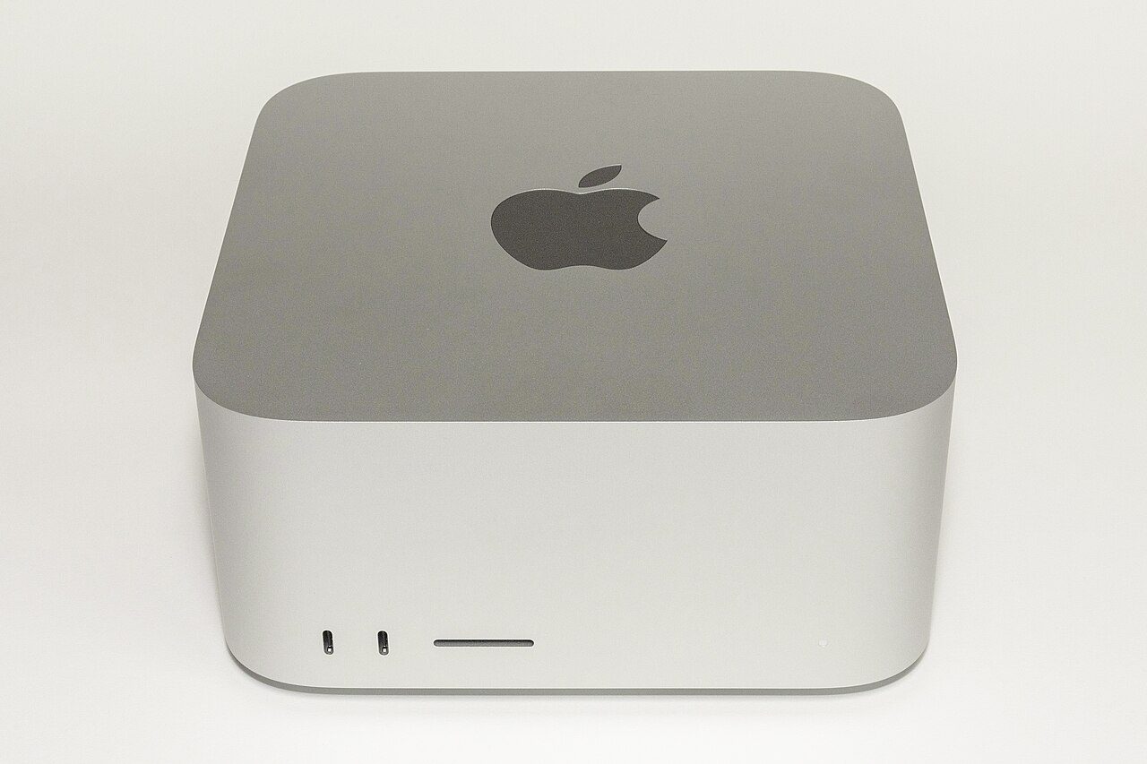 A square, silver aluminum desktop computer with rounded corners and a black Apple logo on top, shown against a plain white background