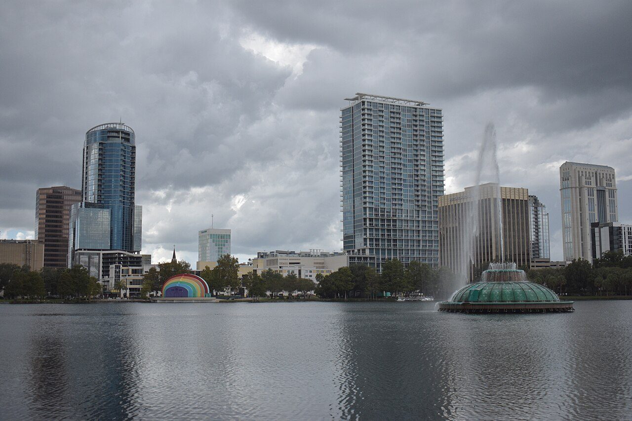 Tall buildings behind a lake with a fountain under a cloudy sky