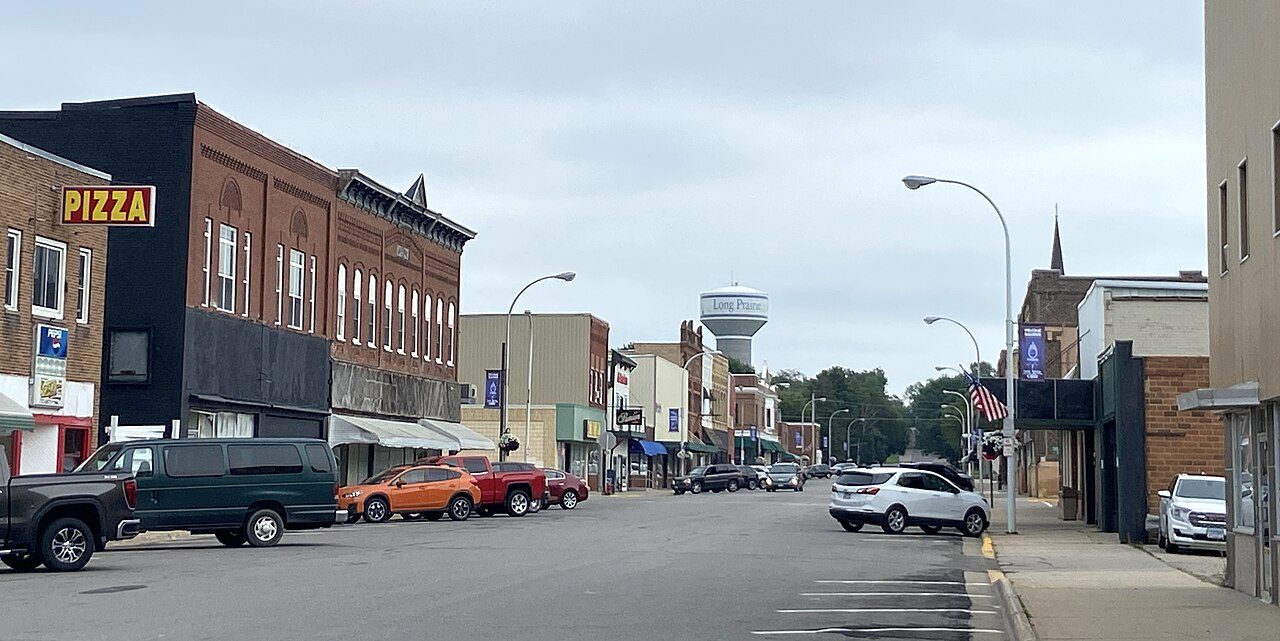 A small-town main street with brick storefronts, parked pickup trucks and a water tower in the distance