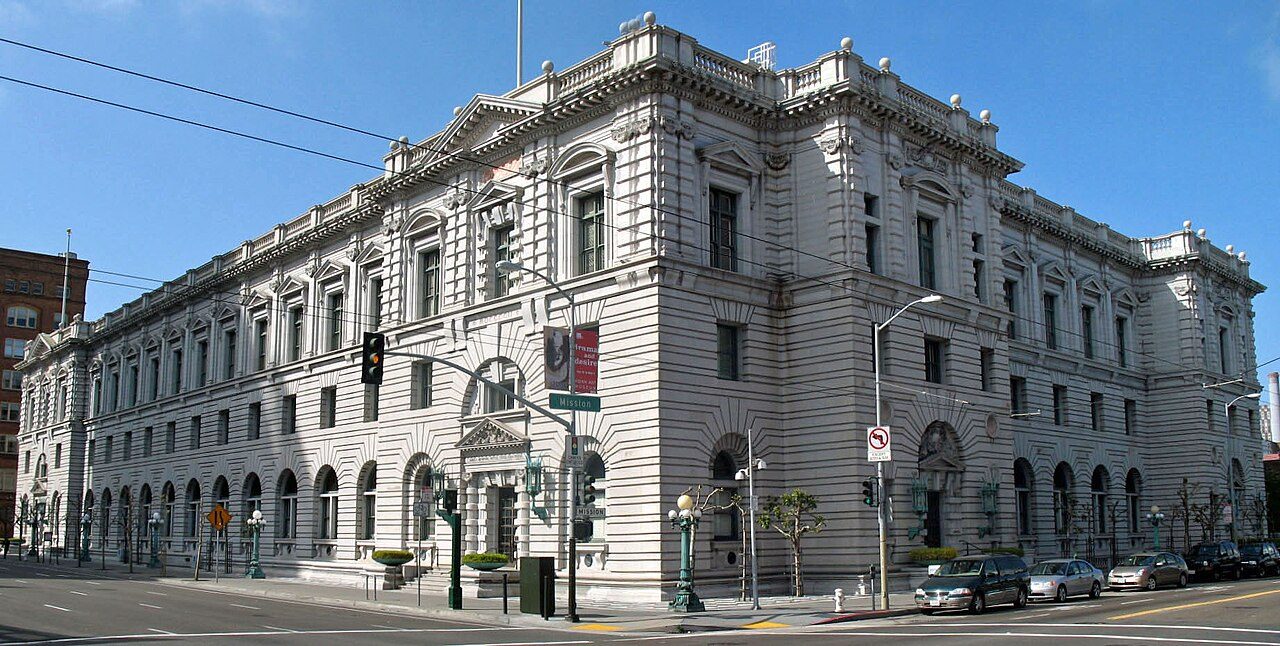 A large stone federal building with arched windows on a city street corner under a blue sky