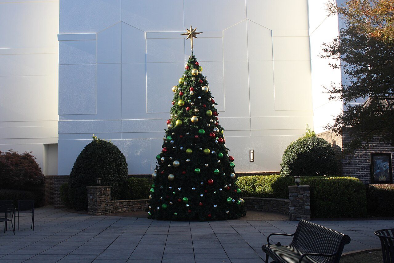 A decorated Christmas tree on a paved plaza outside a large white building