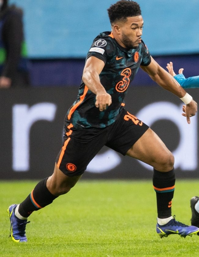 Reece James in a dark Chelsea kit running with the ball on a grass field