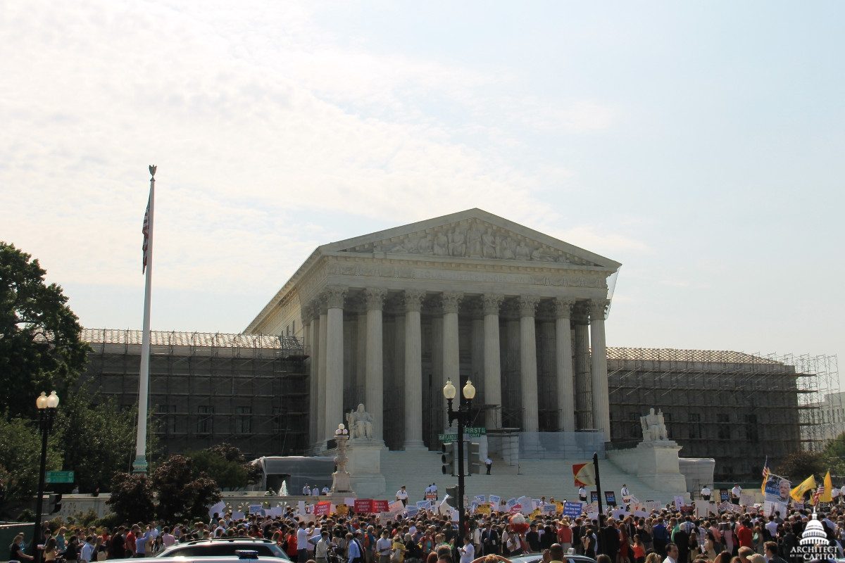 The columned front of the U.S. Supreme Court building with a large crowd and flags on the plaza