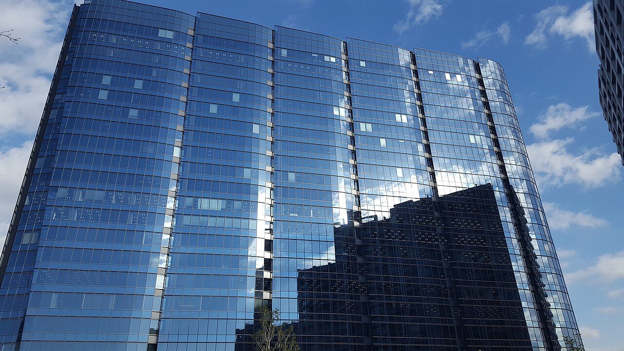 A tall glass office tower reflecting a blue sky with clouds