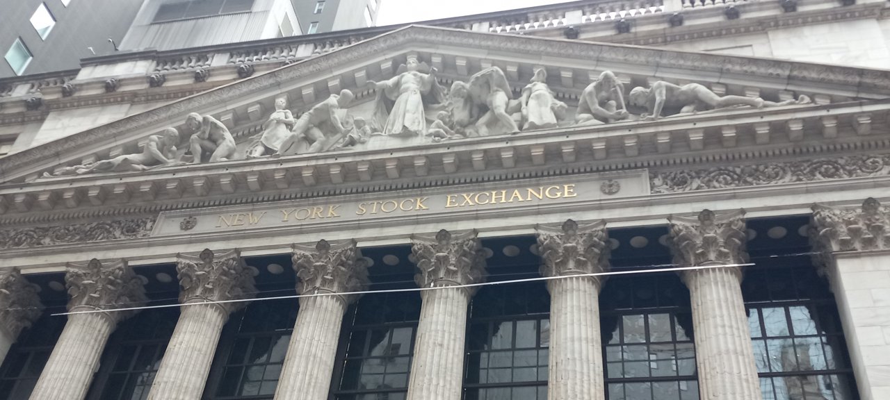 The columned facade of the New York Stock Exchange building, with its name carved in gold letters below a pediment of sculpted figures