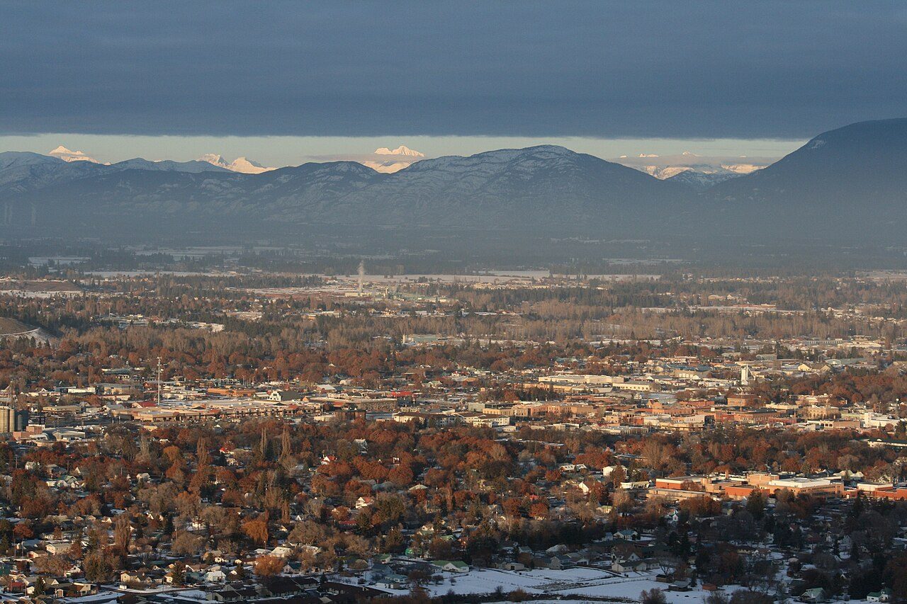 A view over the city of Kalispell in a wide valley with snow-dusted mountains rising in the distance
