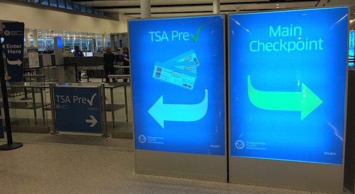 Two lighted blue airport signs, one reading TSA Pre with an arrow pointing left and one reading Main Checkpoint with an arrow pointing right