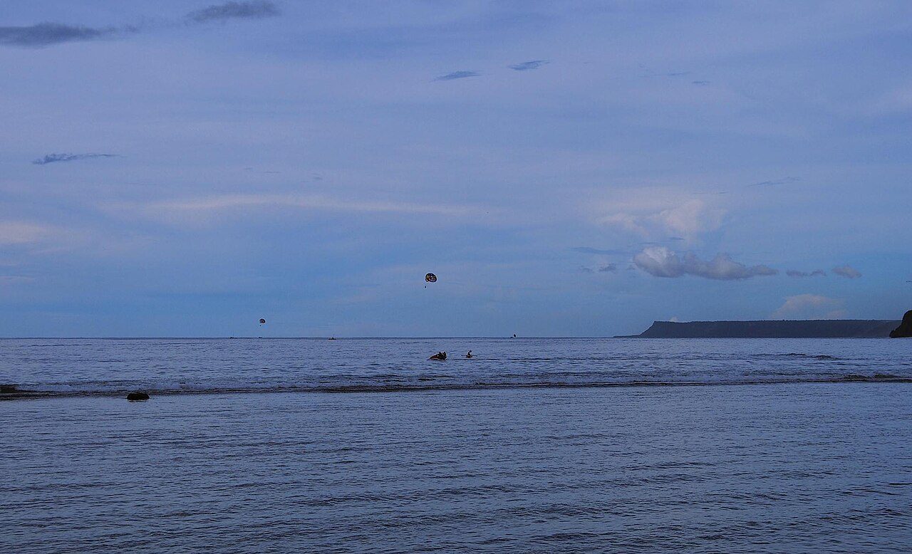 A calm bay of gray-blue water under a cloudy evening sky, with a low green headland on the horizon