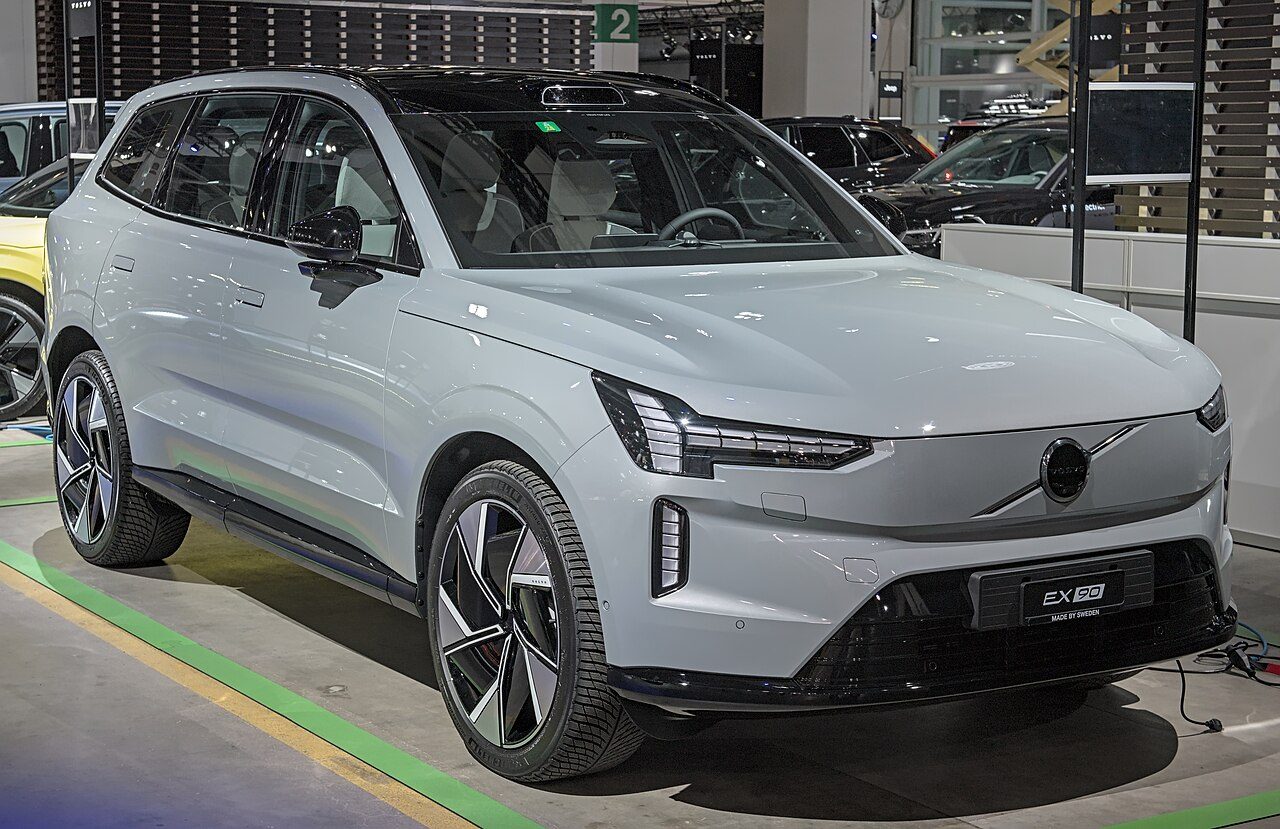 A light gray Volvo EX90 electric SUV parked on display at an indoor auto show