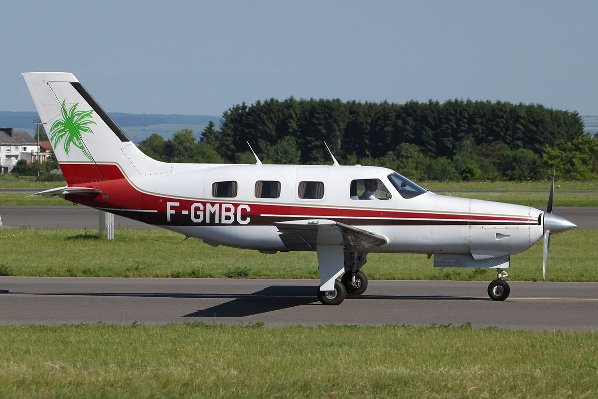 A small white single-engine plane with a red stripe taxiing on a runway beside green grass and trees