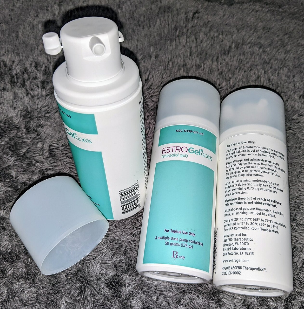 Three white and teal pump bottles of EstroGel estradiol gel, one with its cap off, on a gray surface