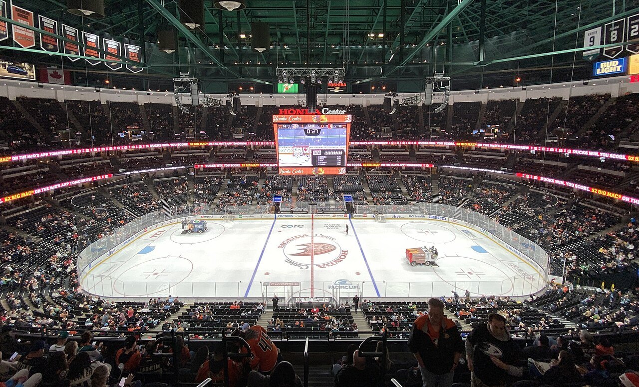 A wide view inside an arena from the upper seats, showing a hockey rink, a large center-hung scoreboard and crowded stands