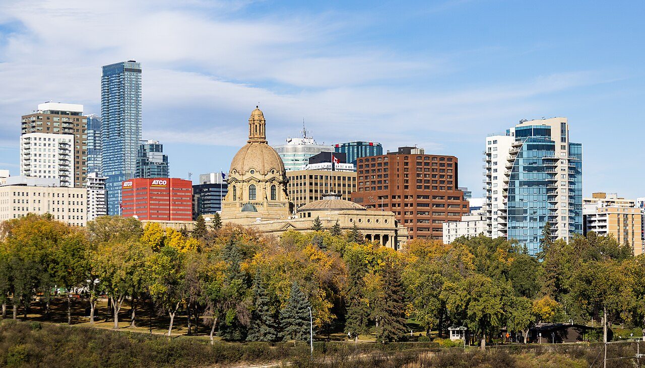 The domed Alberta Legislature Building in Edmonton seen across autumn trees, with downtown office towers behind it