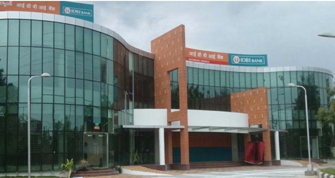 A curved glass-fronted building with orange and blue IDBI Bank signs in Hindi and English above the entrance
