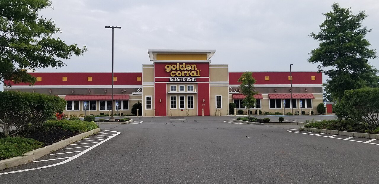 A Golden Corral restaurant with a red and cream front and a large sign, behind an empty parking lot under a cloudy sky
