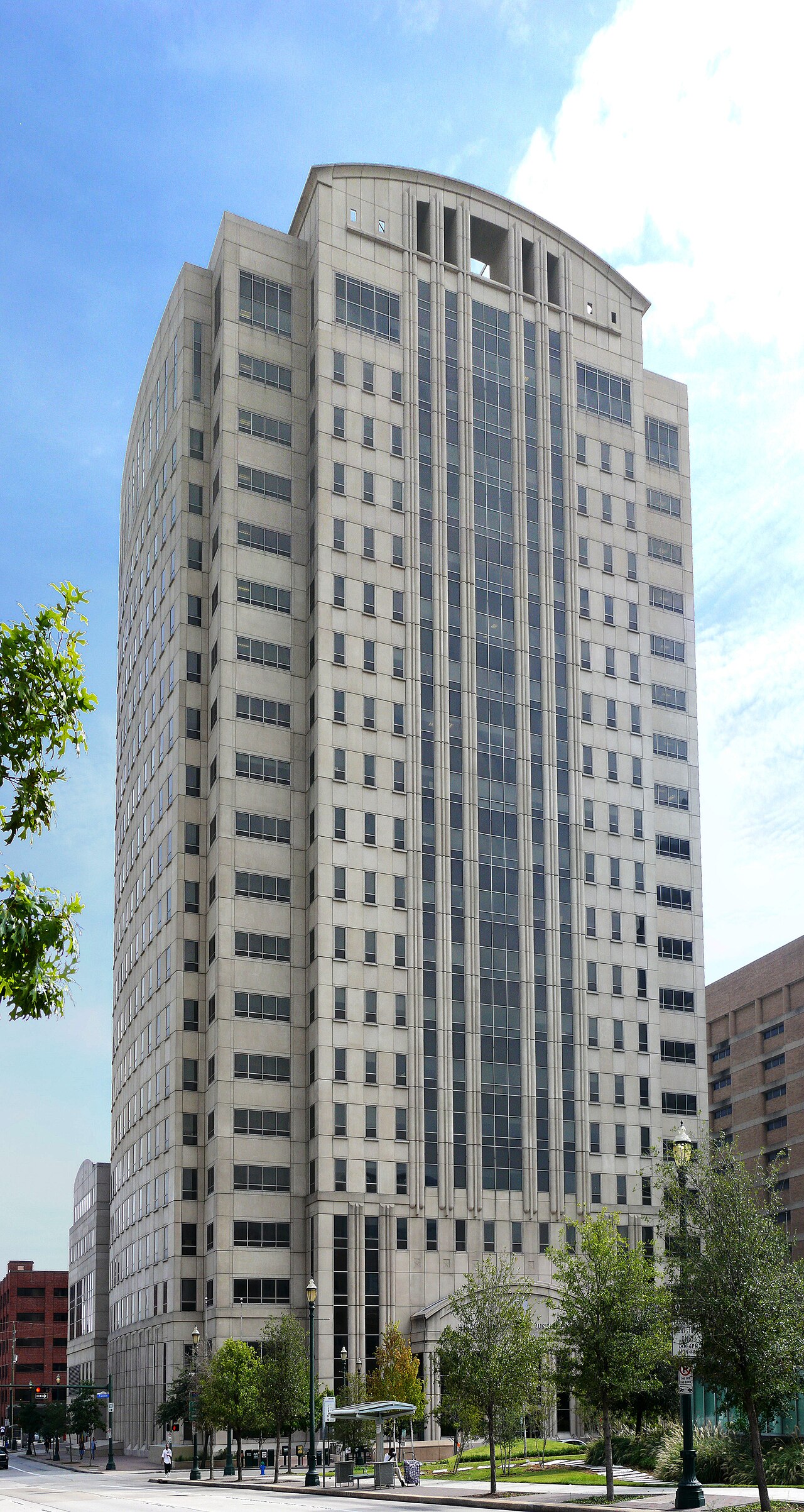 The Harris County Criminal Justice Center, a tall pale stone high-rise with a curved top, on a downtown Houston street under a blue sky