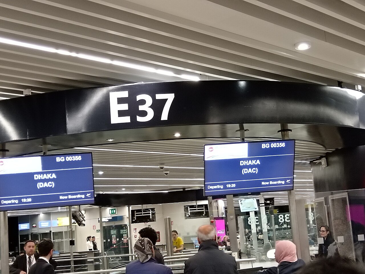 A departure gate area at Rome Fiumicino airport with a large E37 gate sign and screens above seated passengers
