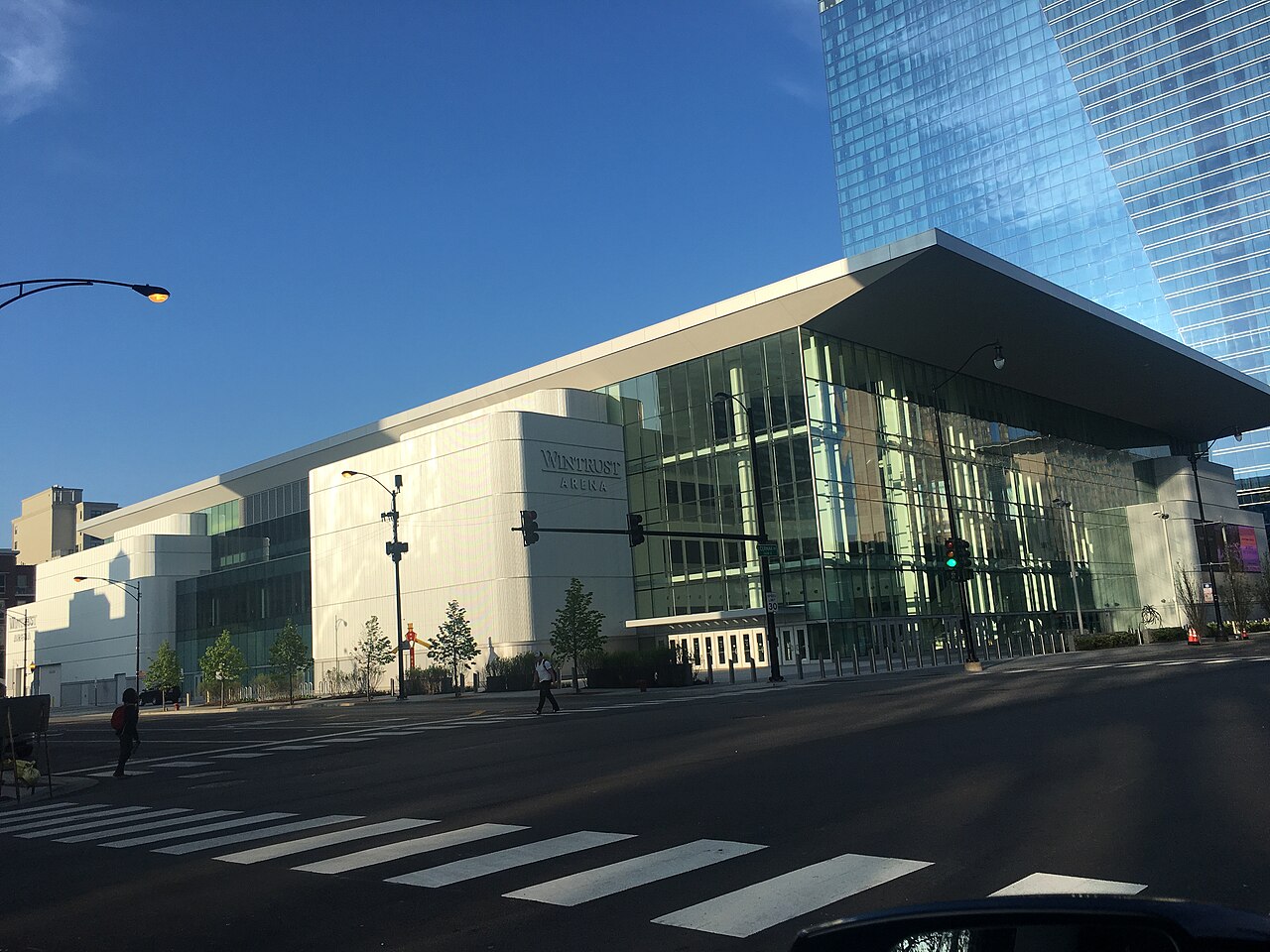 The white and glass exterior of Wintrust Arena in Chicago on a sunny day, seen from across a street with a crosswalk