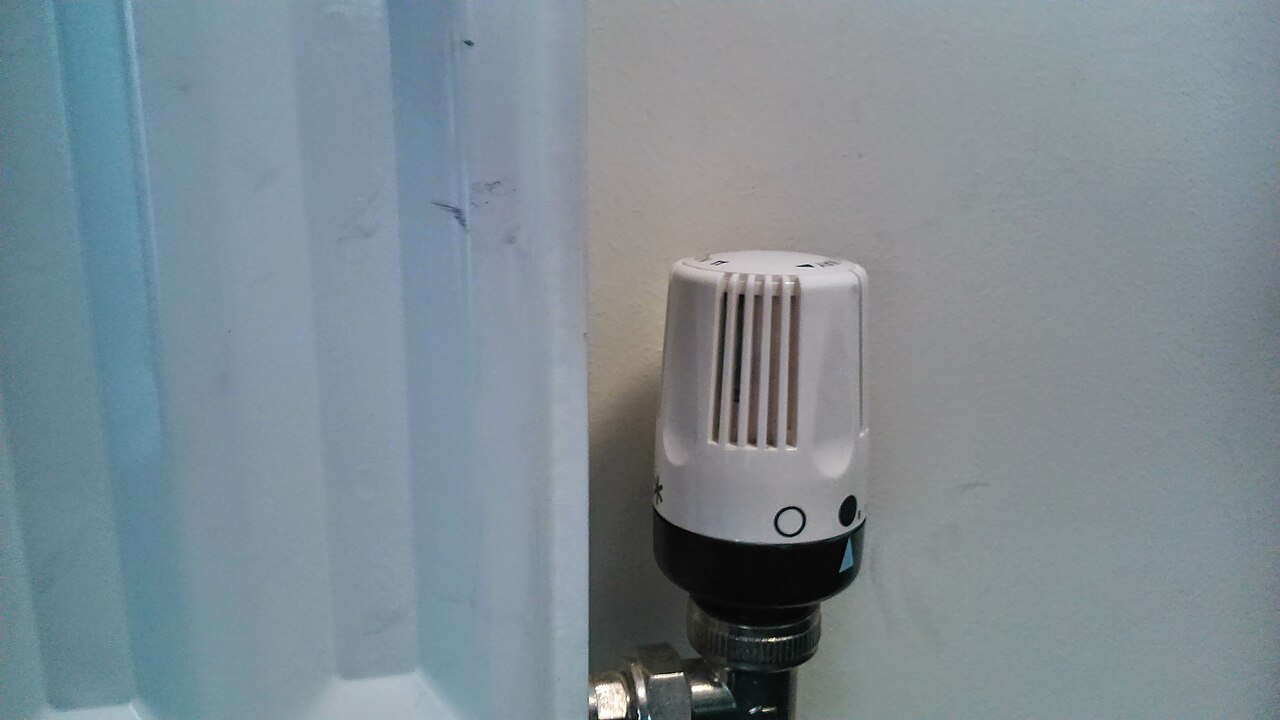 A white thermostatic valve attached to a white radiator against a pale wall