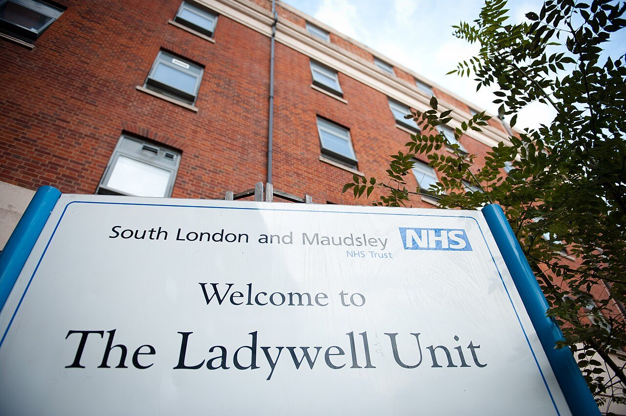 A white NHS trust sign reading Welcome to The Ladywell Unit in front of a red brick hospital building