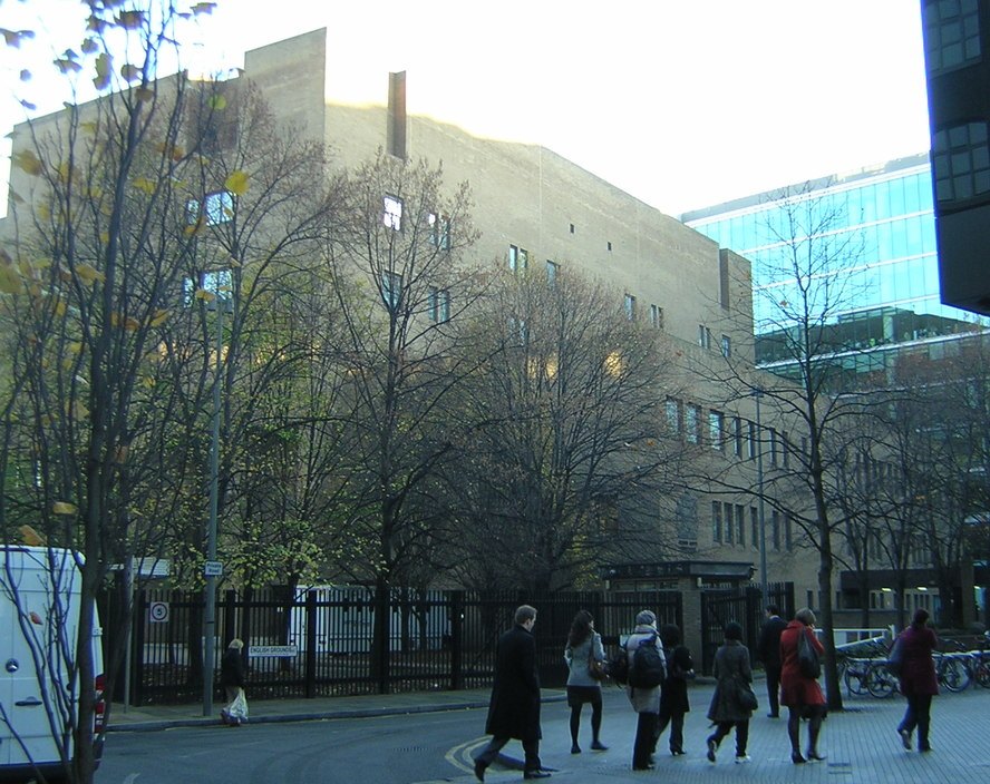 A brick and concrete court building on a London street in winter, with bare trees and people walking past on the pavement