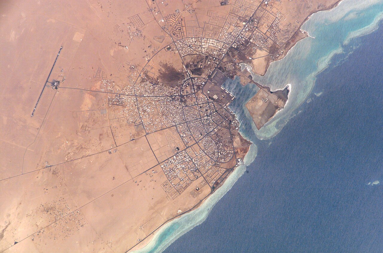 Astronaut photograph of the coastal city of Yanbu on Saudi Arabia's Red Sea coast, showing a street grid, a harbor and a long airport runway in the desert