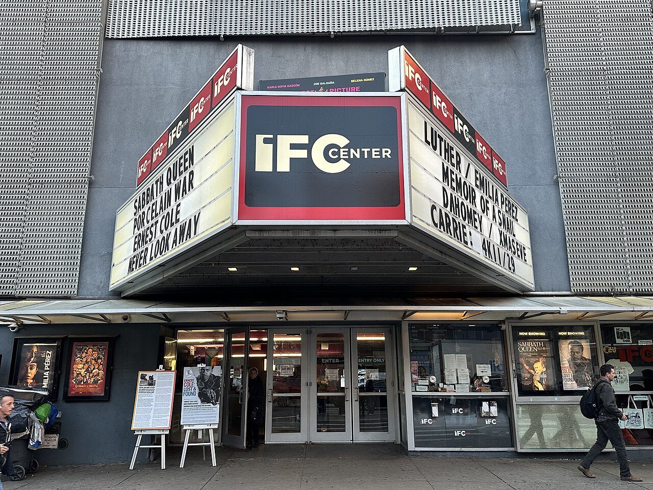 The marquee of the IFC Center cinema in New York, listing film titles above glass entrance doors, with a man walking past