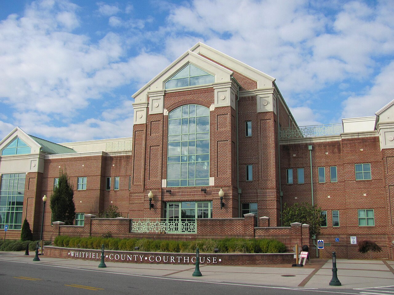 The Whitfield County Courthouse in Dalton, Georgia, a red-brick building with a tall arched glass window under a white gable, beneath a partly cloudy sky