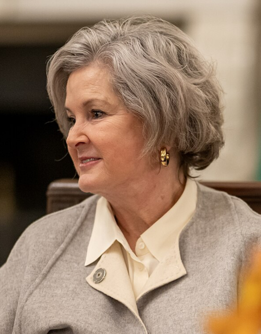 White House chief of staff Susie Wiles, with short gray hair and gold earrings, wearing a light gray jacket over a cream blouse, seated indoors