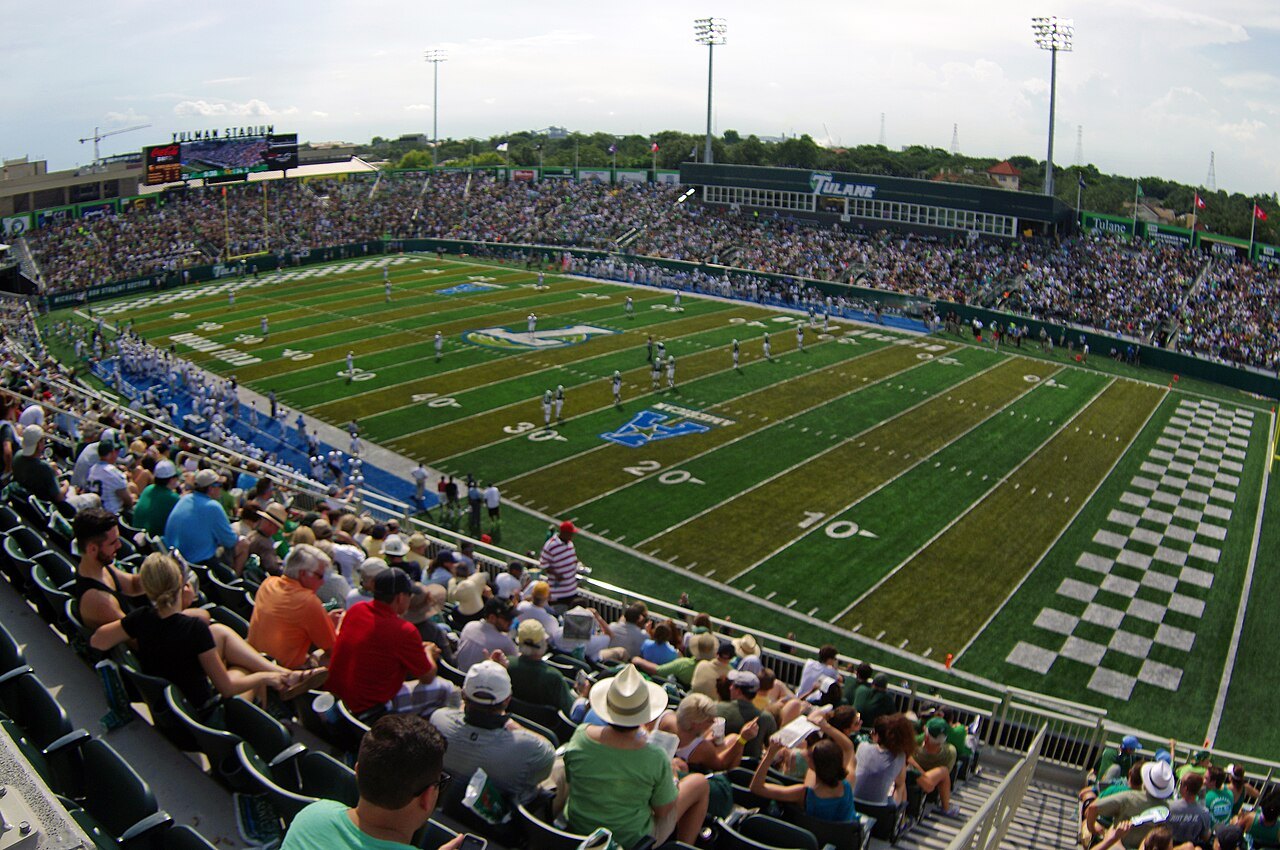 Fans fill the stands at Yulman Stadium, looking down on a green football field with a checkered end zone