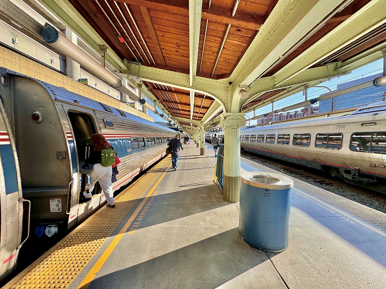 Passengers board a silver Amtrak train from a long covered platform at a train station