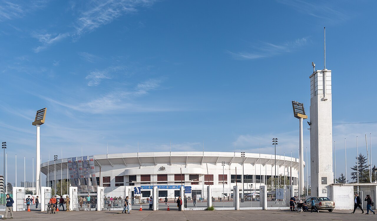 The Estadio Nacional stadium in Santiago, Chile, under a blue sky, with its tower and floodlights