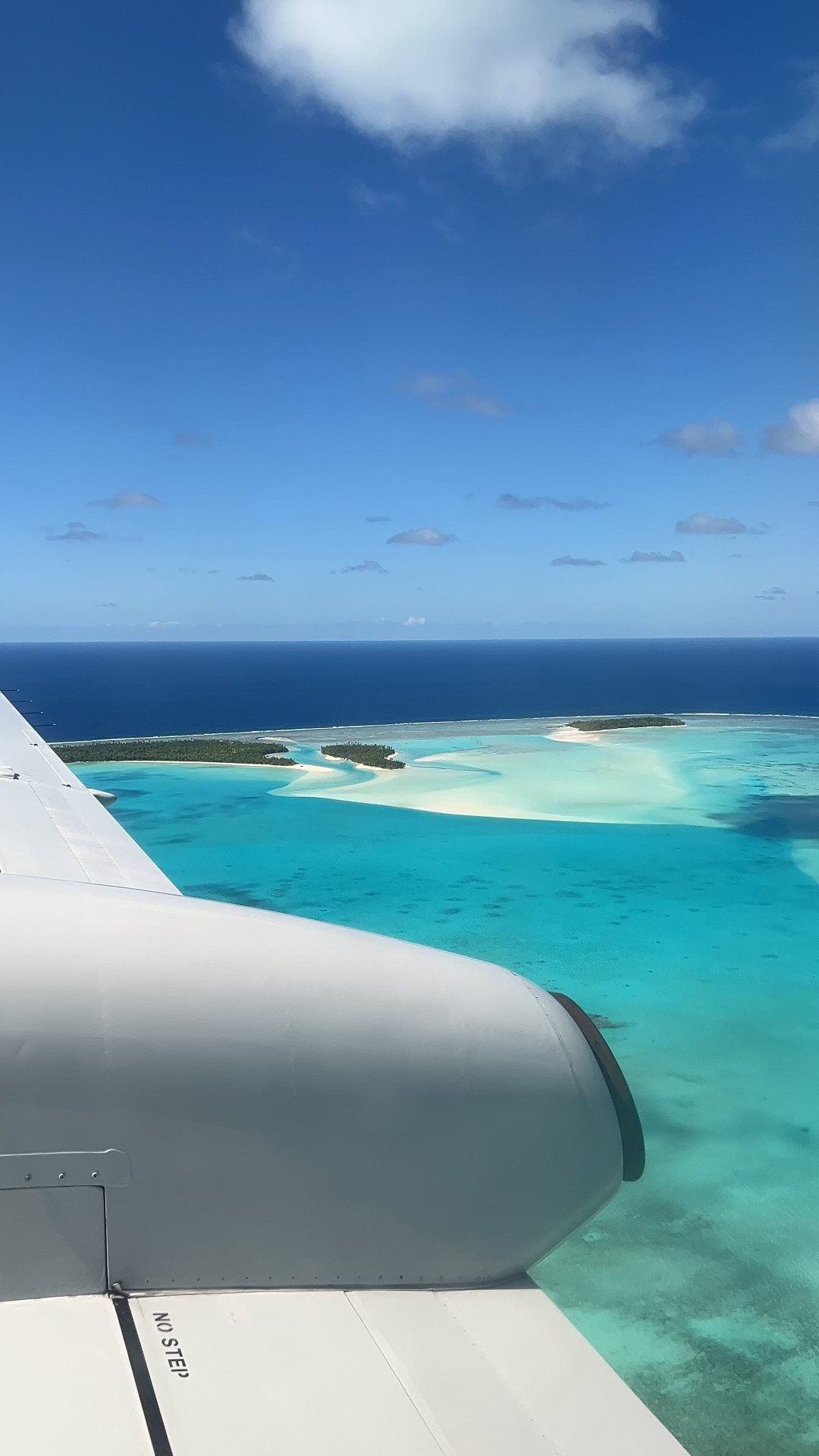 View from an airplane window of a turquoise lagoon with small sandy islands and white surf on a reef