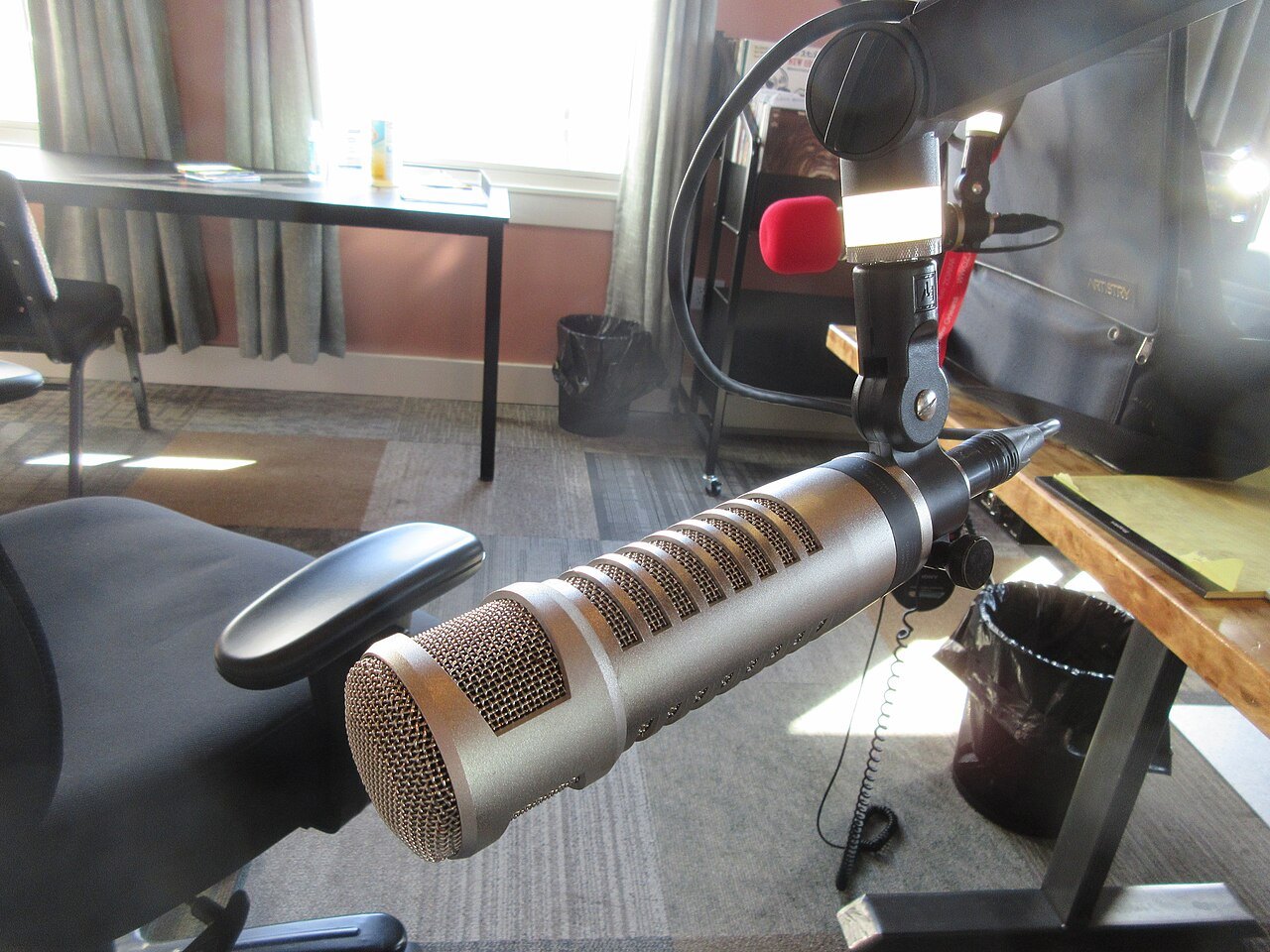 A large silver microphone on an arm in front of a radio studio desk
