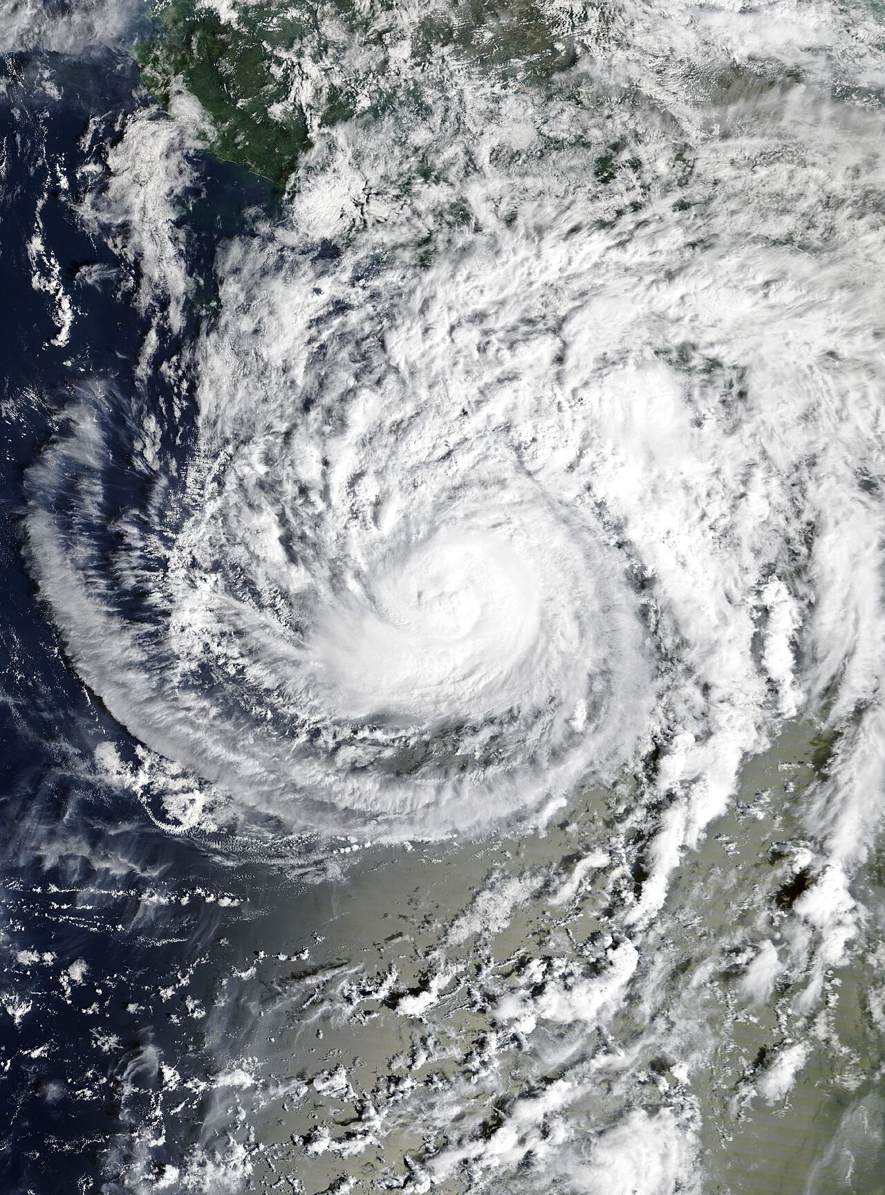 Satellite view of a large hurricane with a tight spiral of white clouds over the dark blue ocean near the coast of Mexico