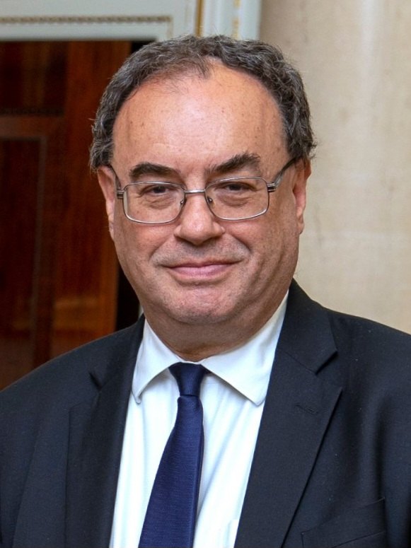Andrew Bailey in glasses, a dark suit and blue tie, smiling indoors