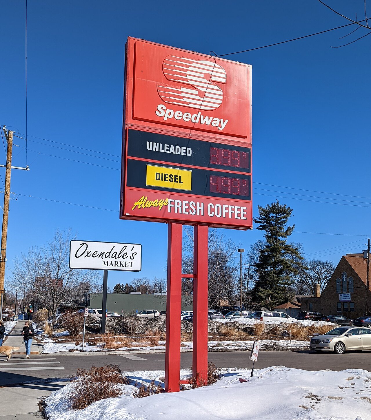 A tall red Speedway gas station sign listing fuel prices stands beside a snowy street under a blue sky