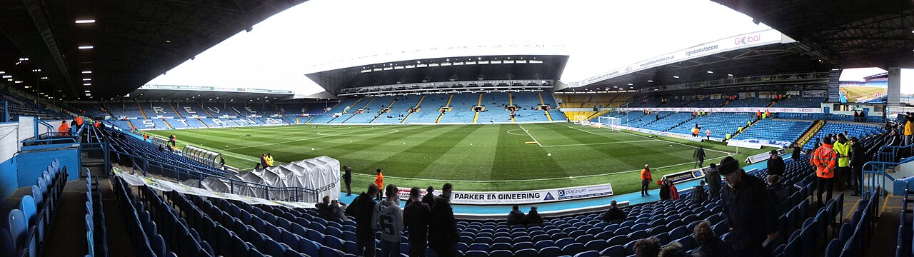 Wide view inside a football stadium with blue seats around a green pitch before a match