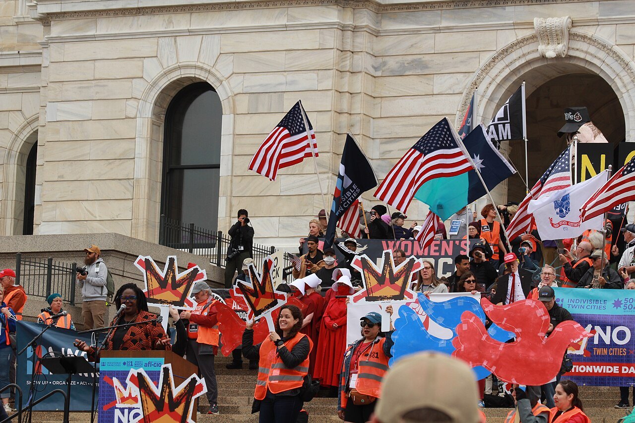 Protesters with US flags, orange vests and signs gather on the steps of a stone government building