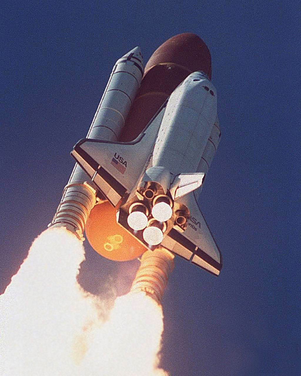 A space shuttle climbs into a deep blue sky on a column of bright orange flame, seen from below