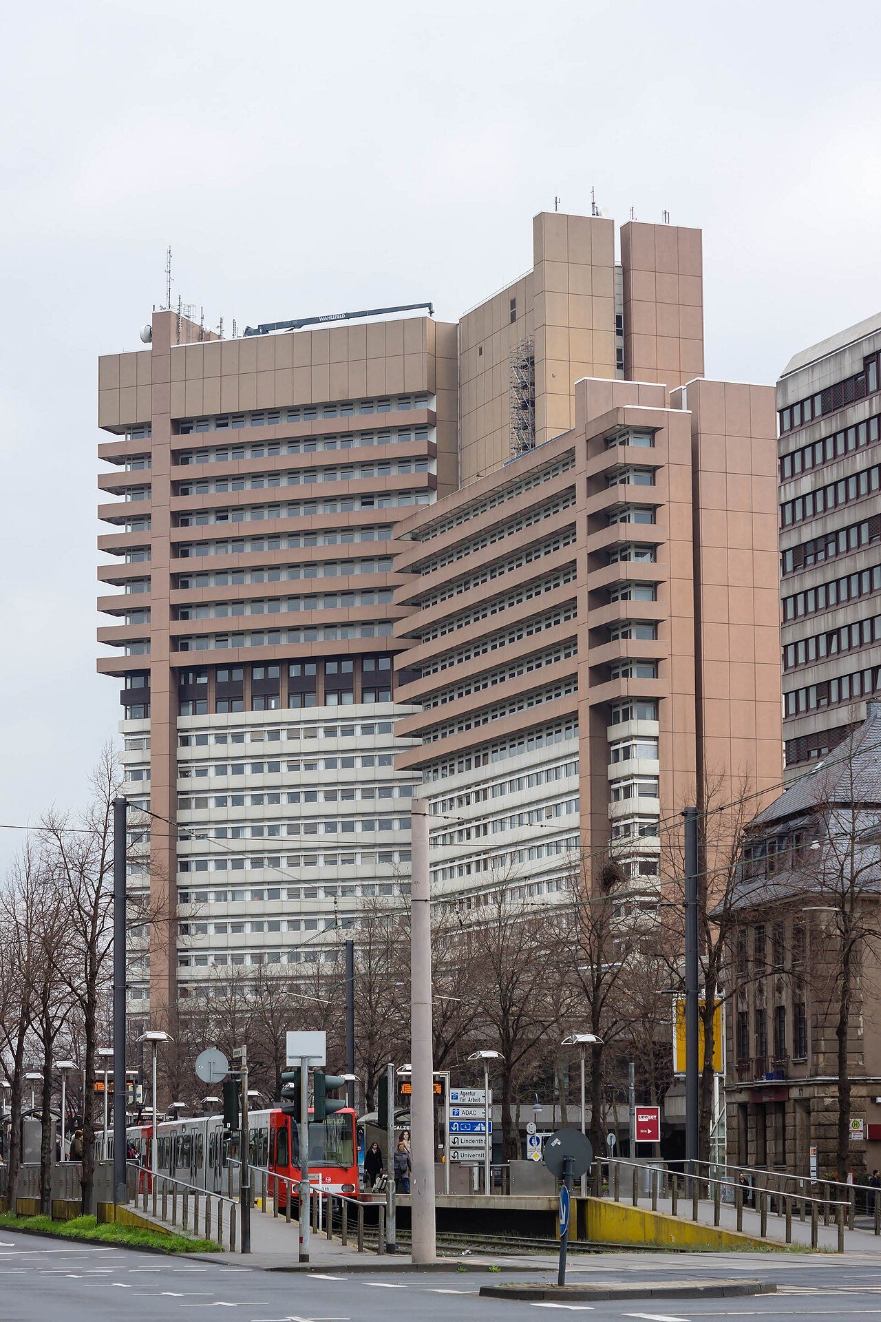Tall modern office towers of a court complex rise behind a street and tram tracks on an overcast day