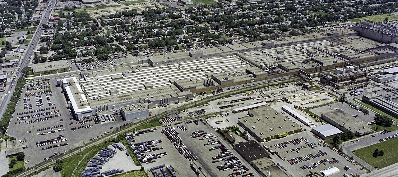 An aerial view of a large car assembly plant with parking lots and rail lines
