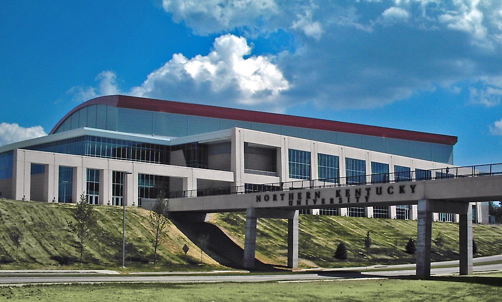 A modern arena with a curved roof and glass front under a cloudy blue sky