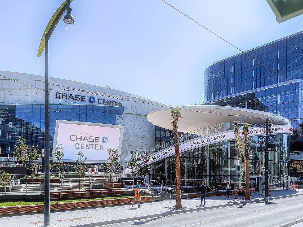 The glass-fronted Chase Center arena in San Francisco with its name on the facade, a plaza and walkways in front