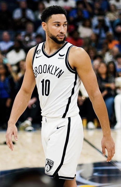 Ben Simmons in a white Brooklyn Nets jersey with the number 10 walks on a basketball court in front of fans