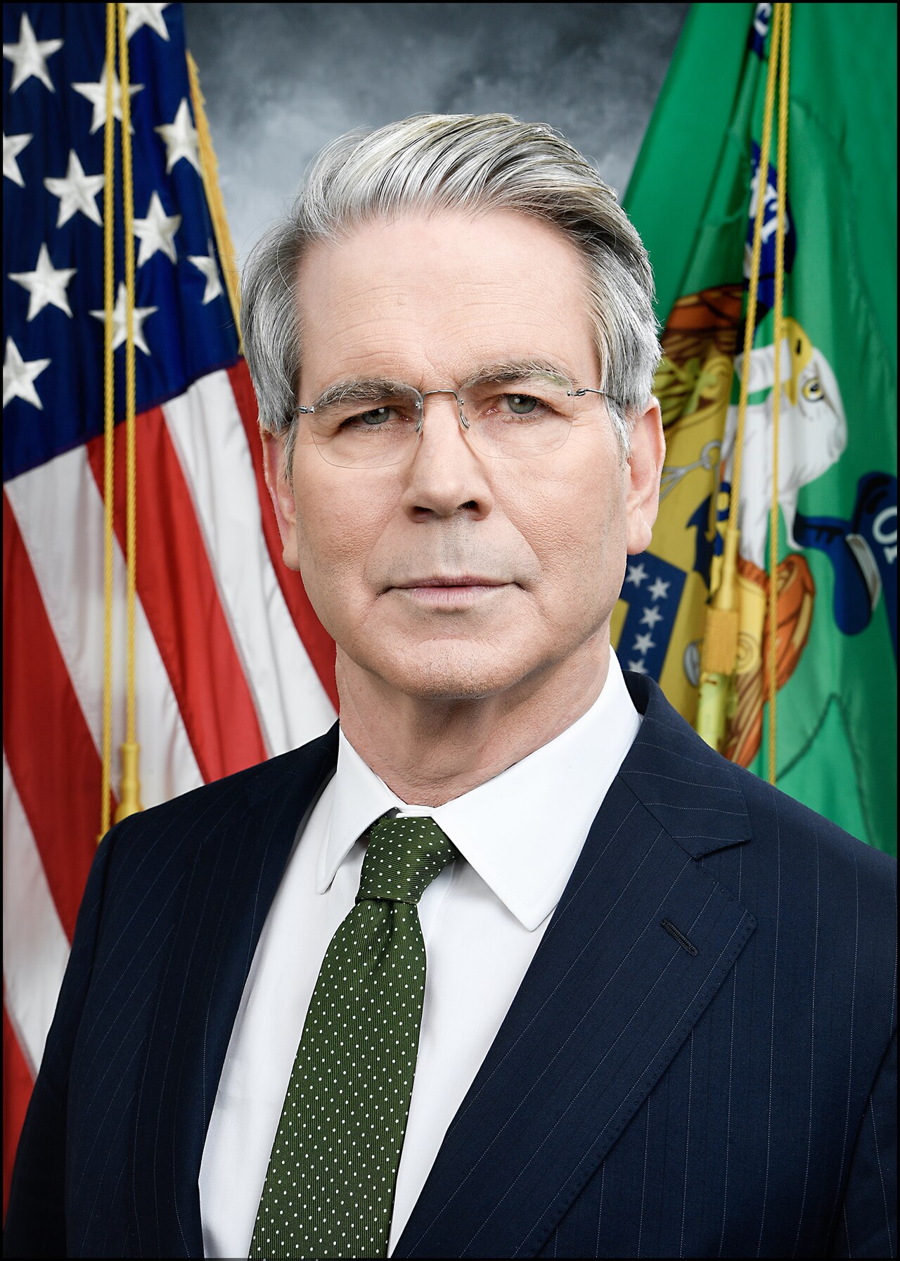 Official portrait of Scott Bessent in a dark suit and green tie, standing in front of a US flag and a green Treasury flag