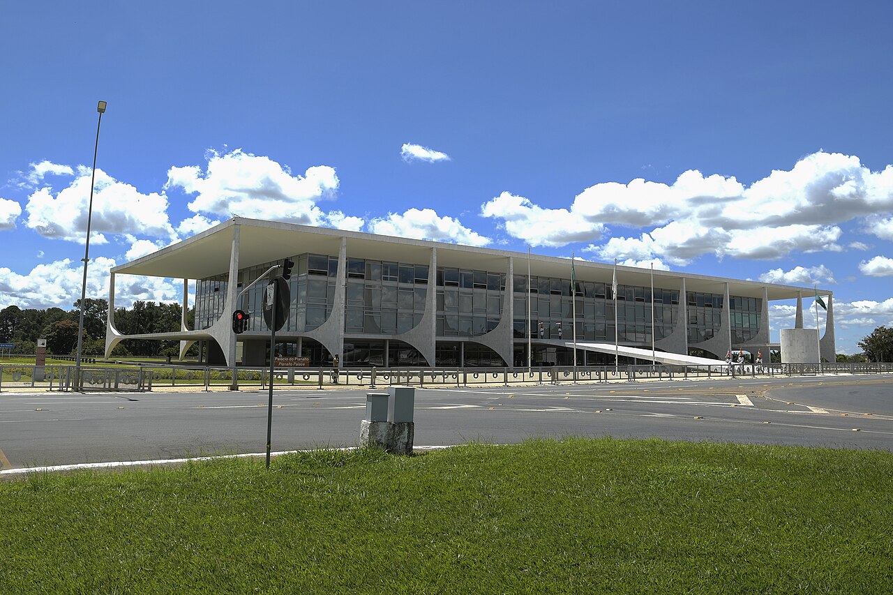 The long white Palácio do Planalto building with slender columns, seen across a green lawn under a blue sky with clouds