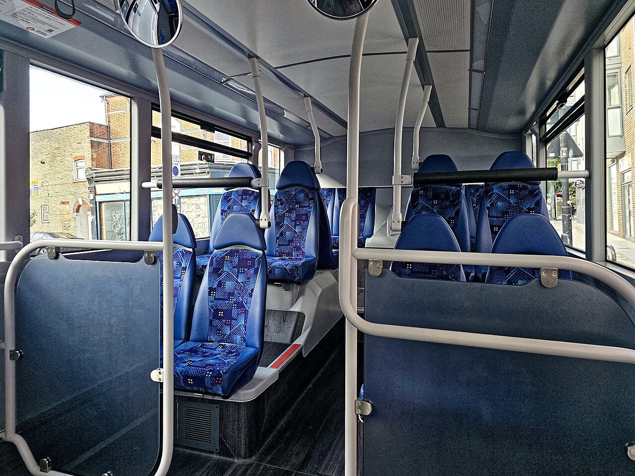 The empty lower deck of a London bus, with blue patterned seats, gray floor and yellow-gray handrails