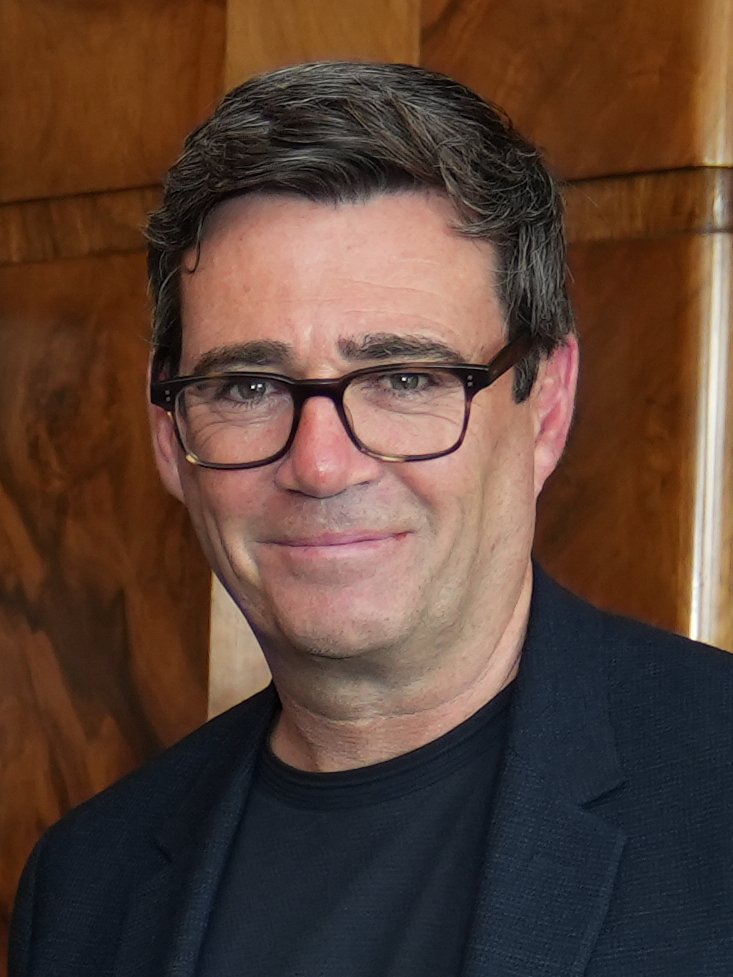Head and shoulders portrait of a smiling man with dark hair and glasses wearing a dark jacket and black shirt