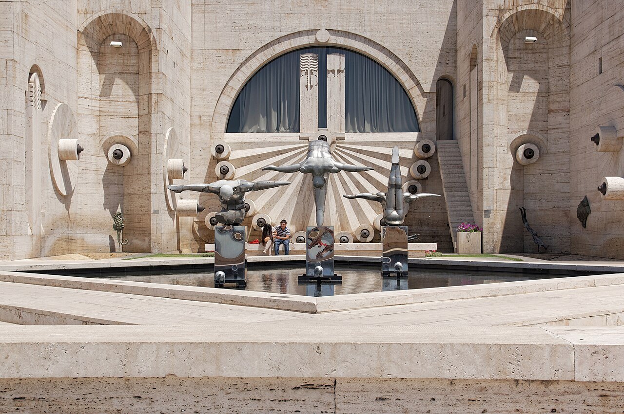 Modern sculptures stand beside a fountain at the foot of a large stone stairway building in Yerevan